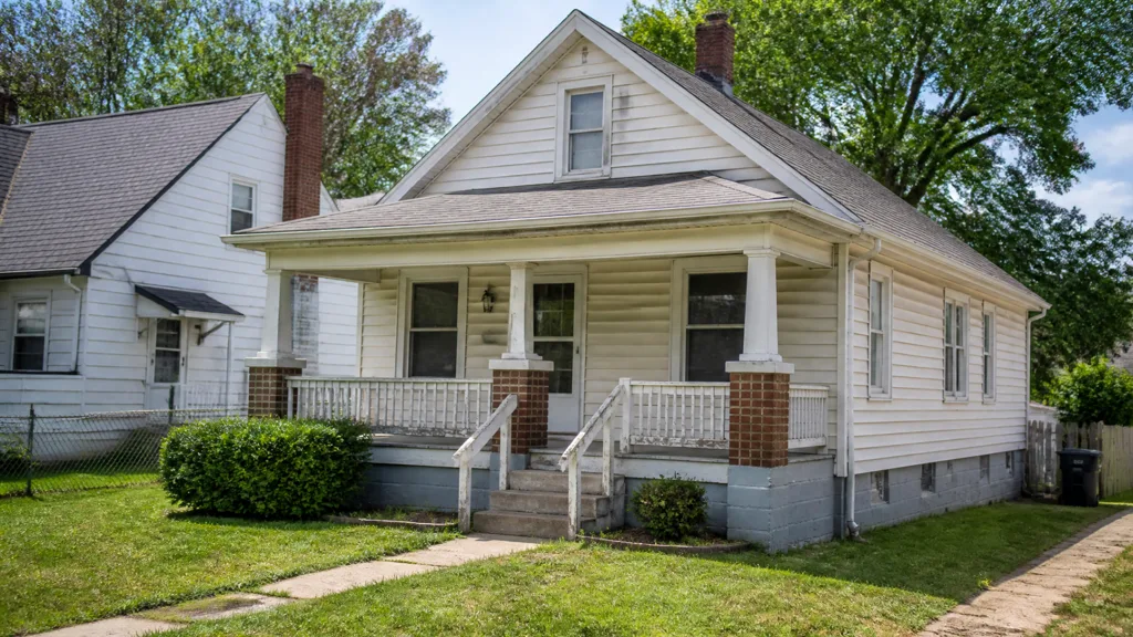 A white bungalow with a covered porch, brick steps and a clipped front lawn.