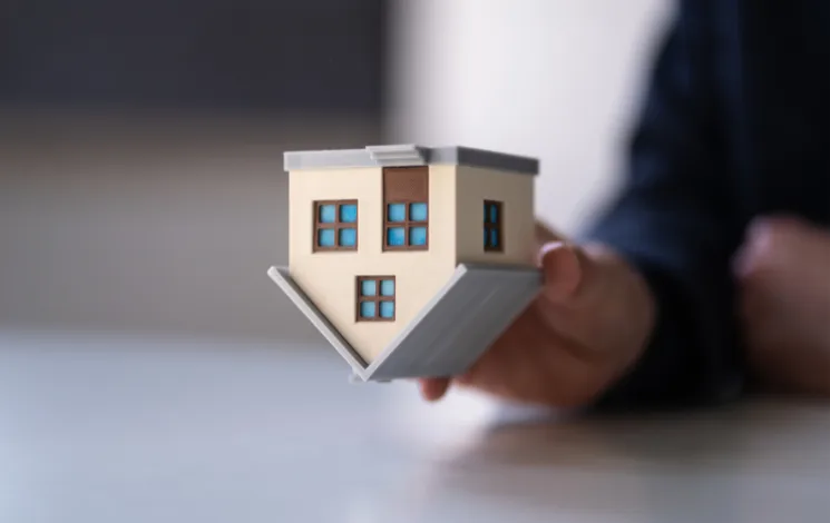 A hand holding a small grey and white model house on a table, seen close up.